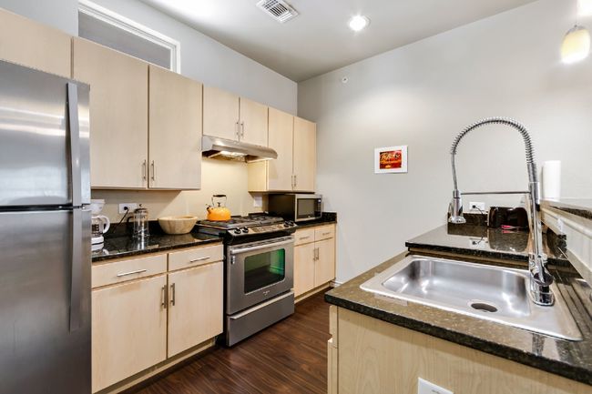 Kitchen featuring stainless steel appliances, under cabinet range hood, dark wood-style flooring, dark stone countertops, and light brown cabinetry | Image 9