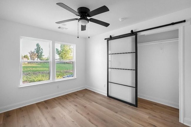 Unfurnished bedroom featuring baseboards, light wood-style flooring, a barn door, and visible vents | Image 12