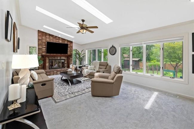 Living room featuring carpet flooring, lofted ceiling with skylight, a fireplace, and a healthy amount of sunlight | Image 8