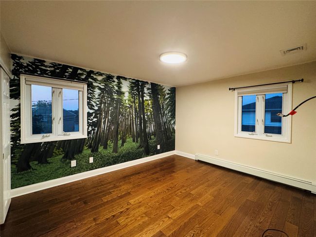 Bedroom with a baseboard heating unit and wood finished floors | Image 9