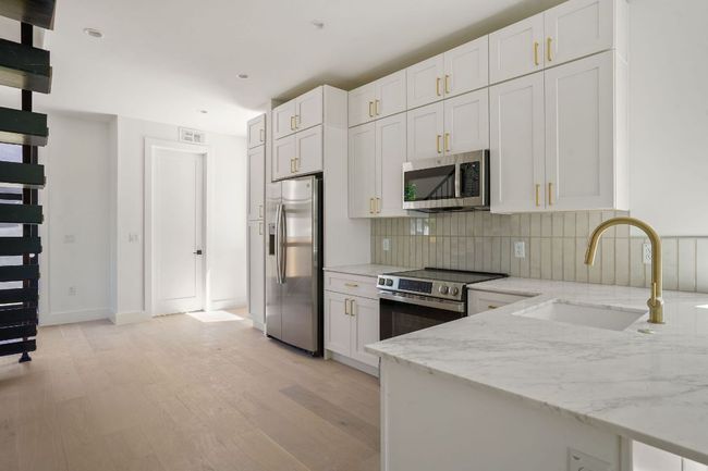 Kitchen featuring light stone countertops, light wood-style flooring, tasteful backsplash, appliances with stainless steel finishes, and a sink | Image 13