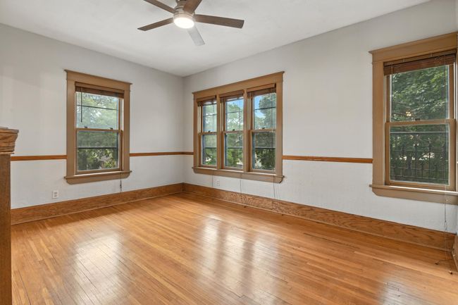 Spacious living area with gleaming hardwood floors, neutral walls, and abundant natural light from multiple windows framed with original wood trim. Ceiling fan adds comfort and style. | Image 12