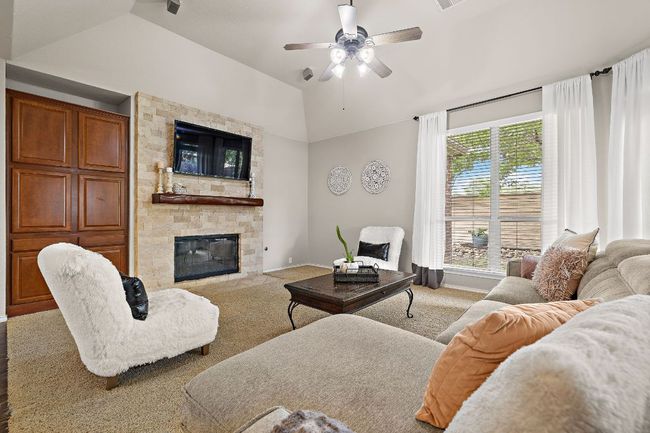 Living area with lofted ceiling, ceiling fan, a fireplace, carpet floors, and baseboards | Image 9