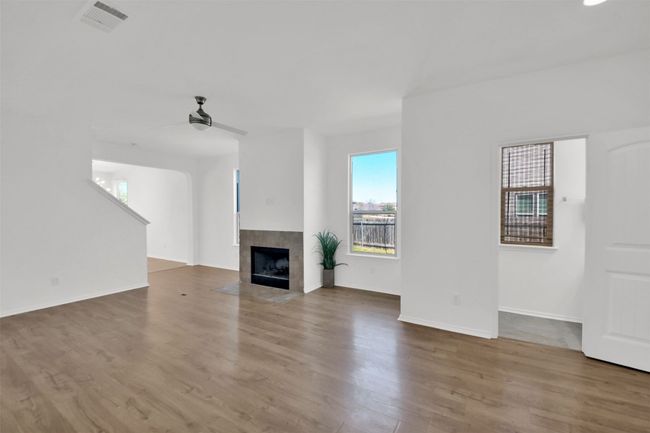 Unfurnished living room with baseboards, visible vents, a ceiling fan, a tile fireplace, and wood finished floors | Image 7