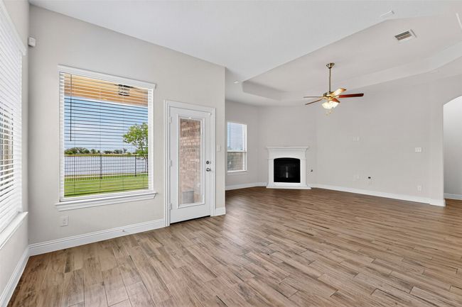Unfurnished living room featuring ceiling fan, light wood finished floors, a glass covered fireplace, arched walkways, and a tray ceiling | Image 12