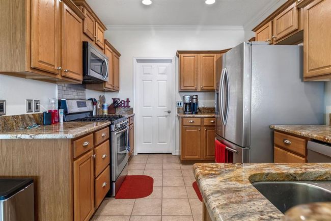 This kitchen features warm wooden cabinetry, granite countertops, and stainless steel appliances. It has a modern design with a tile backsplash and recessed lighting, creating a cozy and functional space. | Image 12