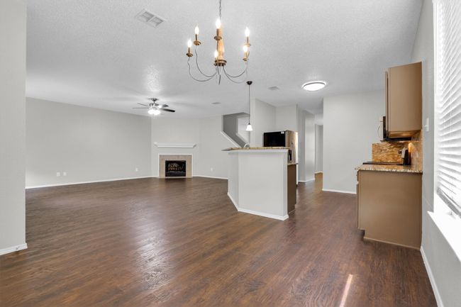 Unfurnished living room with ceiling fan, a textured ceiling, dark wood finished floors, a chandelier, and baseboards | Image 10