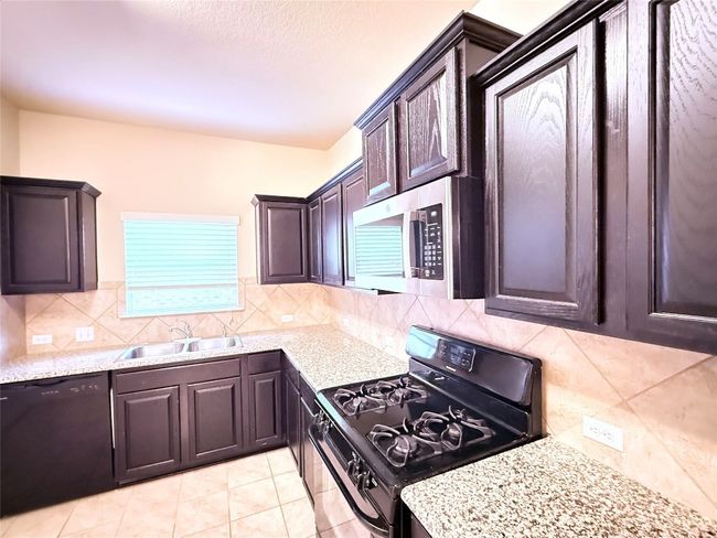 Kitchen featuring range with gas stovetop, decorative backsplash, dishwasher, stainless steel microwave, and dark brown cabinetry | Image 8
