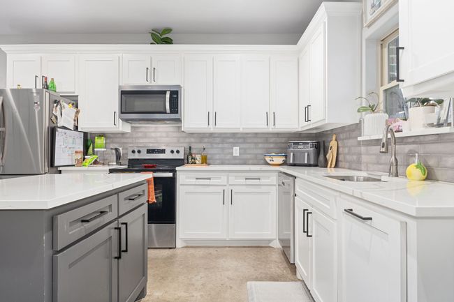 Kitchen with sink, appliances with stainless steel finishes, white cabinetry, gray cabinetry, and light stone countertops | Image 13