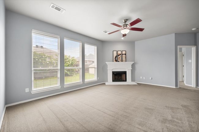 Unfurnished living room featuring carpet floors, a ceiling fan, and a fireplace with raised hearth | Image 9