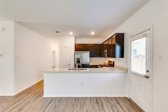 Kitchen featuring stainless steel appliances, a sink, light countertops, light wood-type flooring, and dark brown cabinets | Image 10
