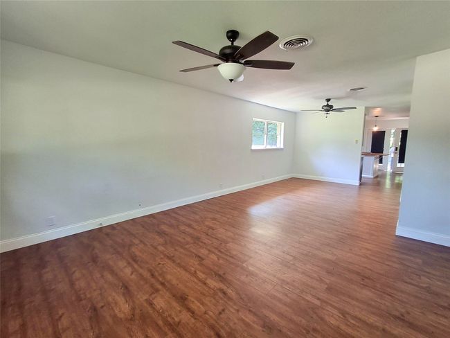 Empty room with dark wood-style flooring, baseboards, and a ceiling fan | Image 13
