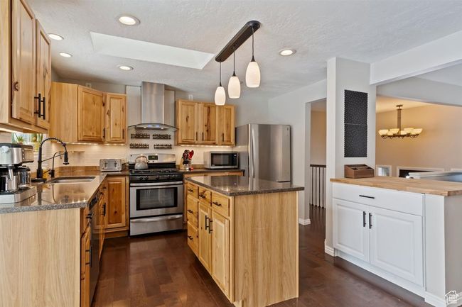 Kitchen featuring wall chimney range hood, stainless steel appliances, a sink, a skylight, and a kitchen island | Image 18