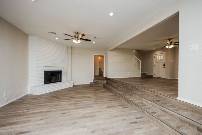 Unfurnished living room featuring ceiling fan, wood finished floors, recessed lighting, a fireplace, and stairway | Image 4