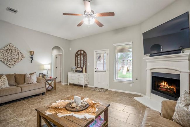 Cozy up in the living room with views of the backyard and a warm corner fireplace. To the left, an arched hallway leads to the spacious primary suite and a nearby bedroom. | Image 16