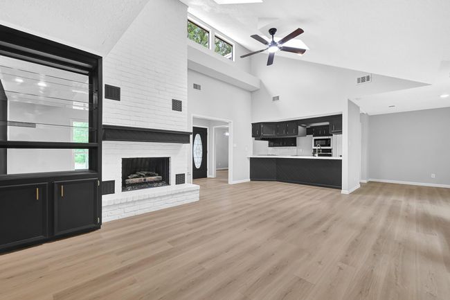 Spacious living area with soaring vaulted ceilings, a stunning white brick fireplace, and a custom built-in bar. Freshly updated with new flooring, recessed lighting, and open sightlines into the beautifully renovated kitchen. | Image 10