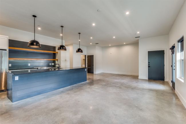 Kitchen featuring concrete flooring, a center island with sink, recessed lighting, dark stone countertops, and decorative light fixtures | Image 5
