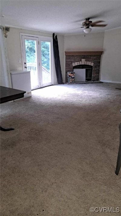 Unfurnished living room with a textured ceiling, carpet, ceiling fan, and a fireplace | Image 2