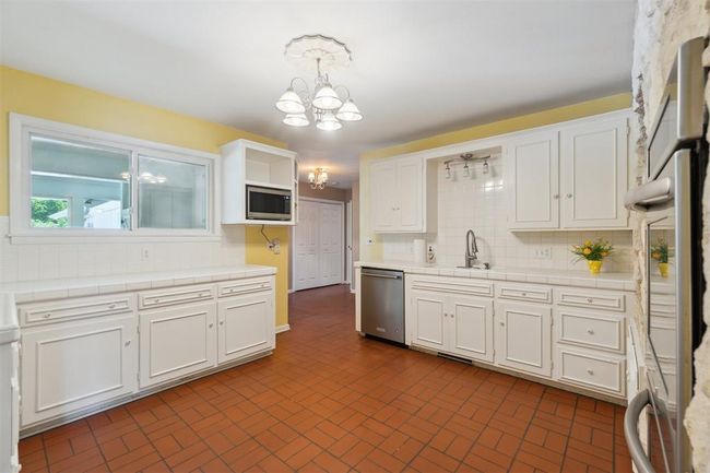 Kitchen featuring appliances with stainless steel finishes, tile counters, a chandelier, and white cabinets | Image 11
