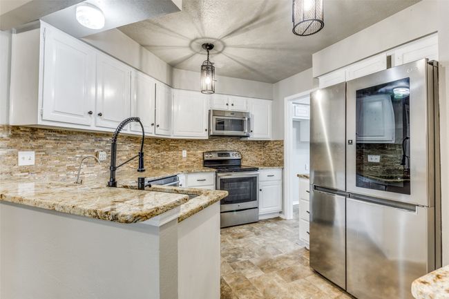 Kitchen featuring appliances with stainless steel finishes, light stone counters, white cabinets, a peninsula, and tasteful backsplash | Image 11