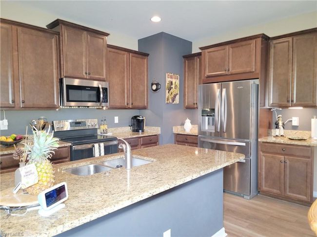 Kitchen with light wood finished floors, light stone countertops, a sink, and appliances with stainless steel finishes | Image 12