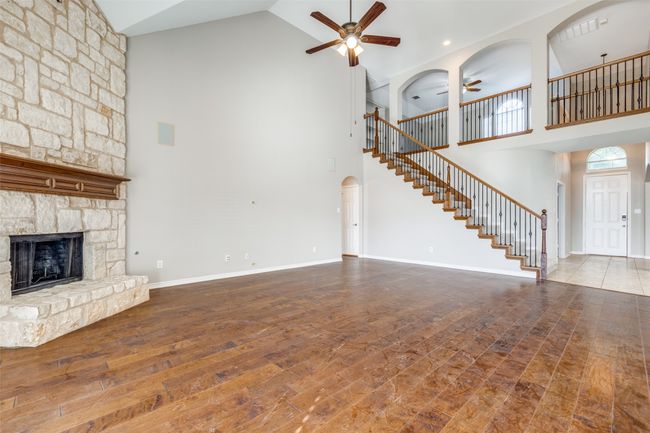 Unfurnished living room featuring stairway, wood finished floors, a ceiling fan, a fireplace, and high vaulted ceiling | Image 7