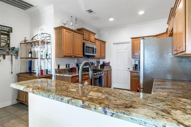 This kitchen features elegant granite countertops, stainless steel appliances, and warm wooden cabinetry. It offers a cozy, functional space with ample storage and modern lighting. | Image 13