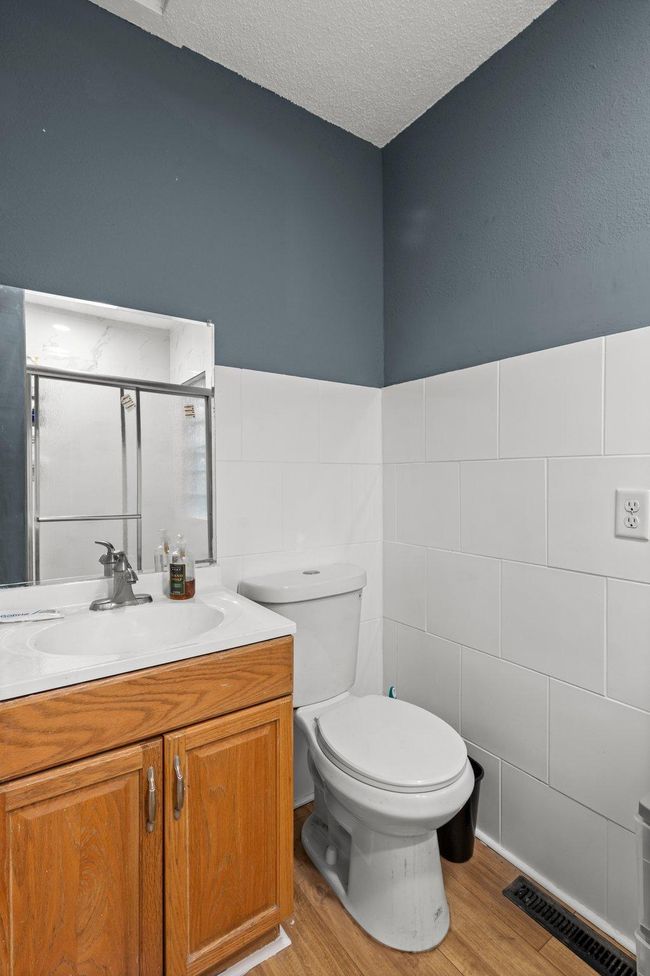 The shared three-quarter bathroom features luxury plank flooring, a single vanity with storage, and a walk-in shower with tile surround. | Image 9