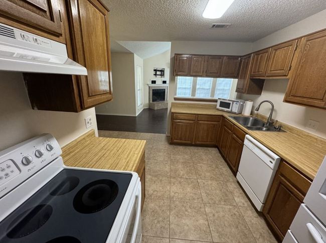 Kitchen featuring a textured ceiling, white appliances, sink, and light tile flooring | Image 10