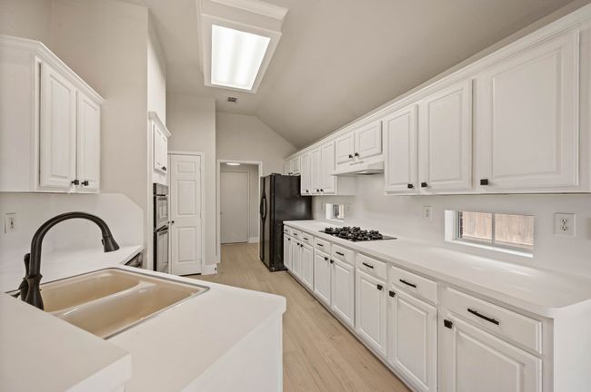 Kitchen featuring a sink, white cabinets, lofted ceiling, under cabinet range hood, and black appliances | Image 13