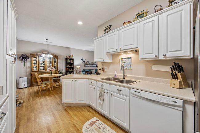 Kitchen with white dishwasher, a sink, light countertops, white cabinets, and light wood-style flooring | Image 4