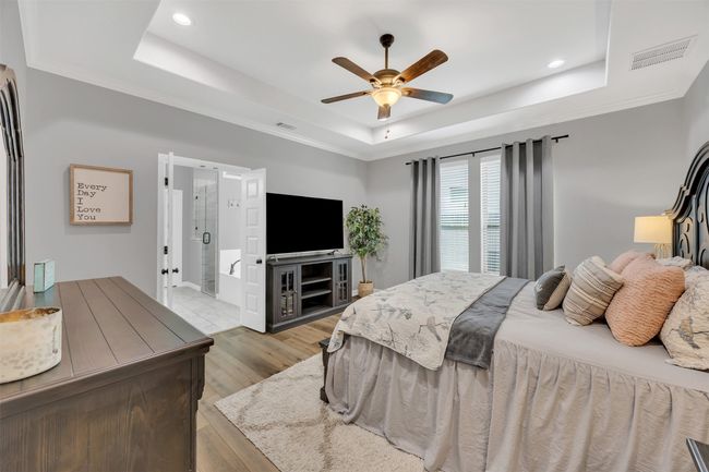 Bedroom with visible vents, a tray ceiling, light wood-style flooring, ceiling fan, and crown molding | Image 18