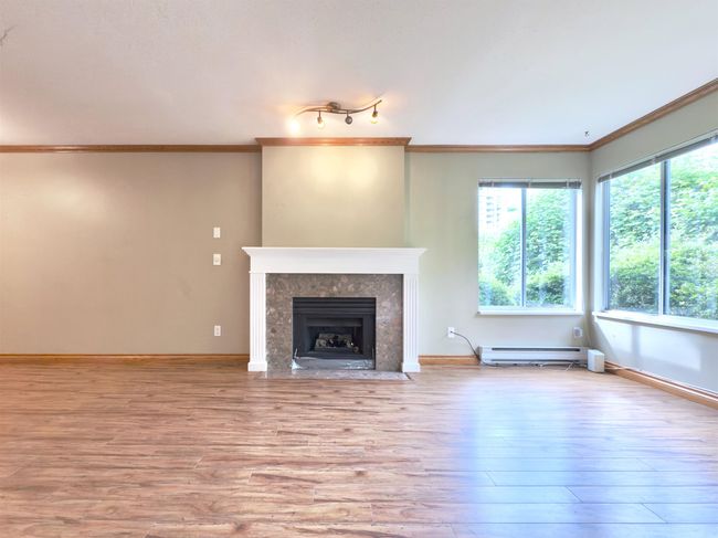 Unfurnished living room featuring crown molding, a baseboard heating unit, wood finished floors, a high end fireplace, and baseboards | Image 4
