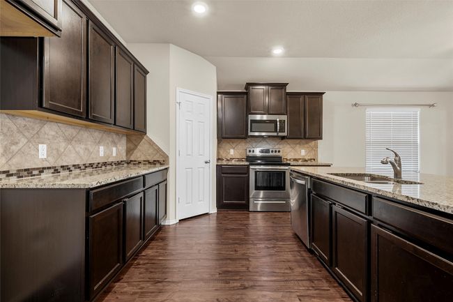 Kitchen with stainless steel appliances, light stone countertops, dark brown cabinets, dark wood-type flooring, and recessed lighting | Image 10