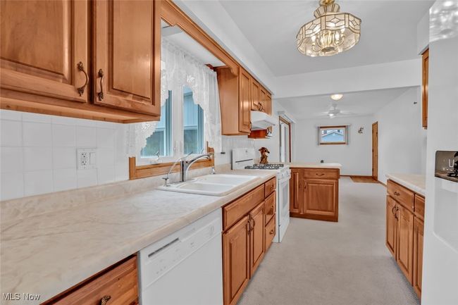 Kitchen featuring white appliances, a sink, backsplash, under cabinet range hood, and a chandelier | Image 12