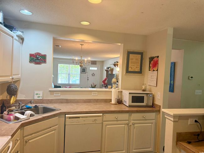 Kitchen with white appliances, white cabinetry, light countertops, hanging light fixtures, and a chandelier | Image 5