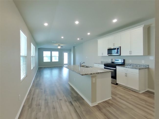 Kitchen with stainless steel appliances, light wood-style flooring, a kitchen island with sink, white cabinets, and light stone countertops | Image 5