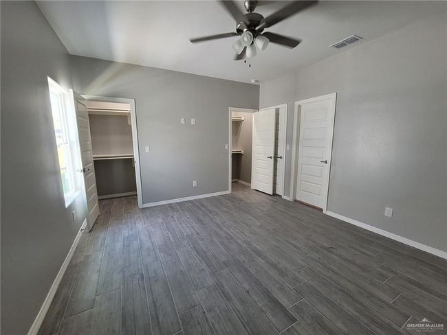 Unfurnished bedroom with baseboards, visible vents, a walk in closet, and dark wood finished floors | Image 5