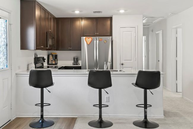 Kitchen with black appliances, dark brown cabinetry, a kitchen bar, light countertops, and recessed lighting | Image 12