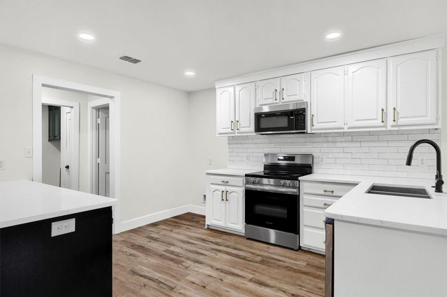 Kitchen with appliances with stainless steel finishes, a sink, tasteful backsplash, light wood-type flooring, and white cabinets | Image 9