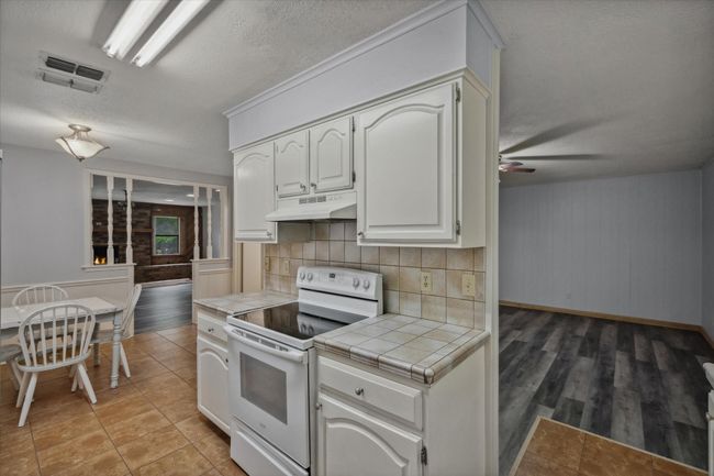Kitchen with white electric stove, under cabinet range hood, tile counters, a ceiling fan, and tasteful backsplash | Image 22