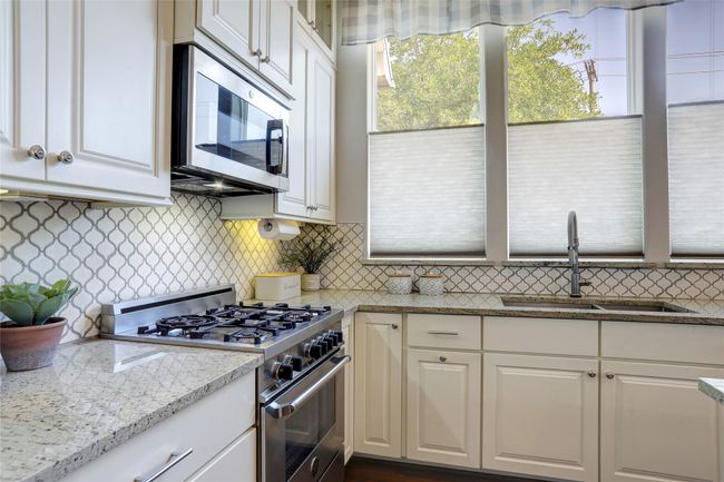 Kitchen with gas cooktop, the microwave is also a convection oven, decorative backsplash, and light stone countertops. | Image 6