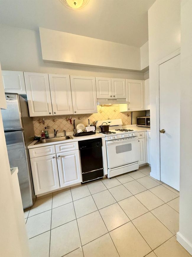 Kitchen with stainless steel appliances, decorative backsplash, white cabinets, and a sink | Image 8