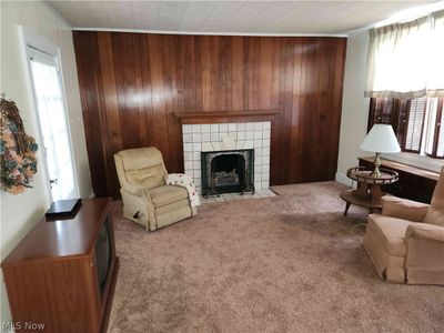 Living room with carpet flooring, wood walls, a tiled fireplace, and crown molding | Image 3