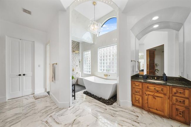 Luxury awaits you in this spa-like private bath with high ceiling, arched openings, dual dressing areas with wood-stained cabinets, granite counters with integrated back splashes and wall mounted mirrors.. | Image 21