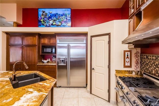 Kitchen with built in refrigerator, under cabinet range hood, black microwave, light tile patterned floors, and light stone counters | Image 36