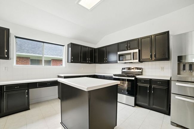 The remodeled kitchen is a true centerpiece, showcasing freshly painted cabinetry with designer hardware, abundant counter and cabinet space, a center island, built-in workstation, and brand-new stainless steel oven/range and microwave. | Image 5