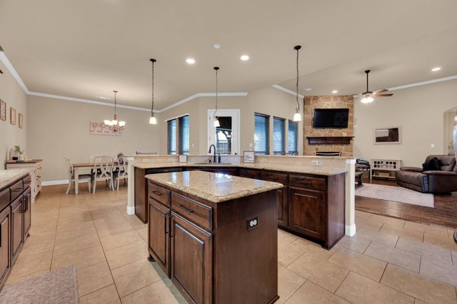 Kitchen with a sink, a large island, crown molding, light tile patterned floors, and dark brown cabinets | Image 6