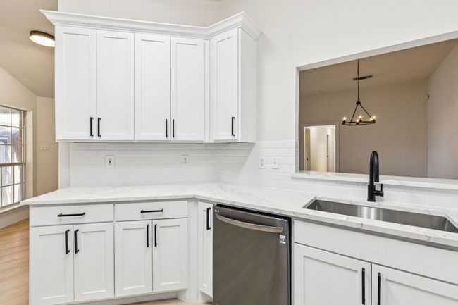 Kitchen with dishwasher, backsplash, white cabinets, light stone countertops, and pendant lighting | Image 4
