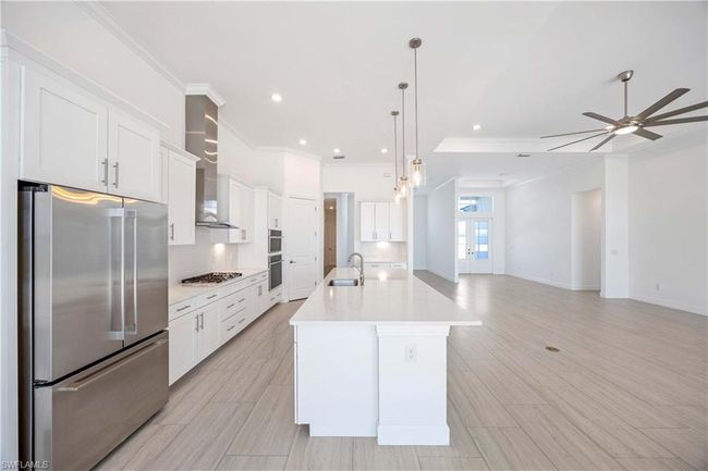 Kitchen with light countertops, a sink, a ceiling fan, appliances with stainless steel finishes, and wall chimney exhaust hood | Image 11